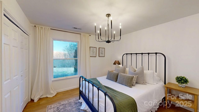 bedroom with a notable chandelier, wood finished floors, visible vents, baseboards, and a closet