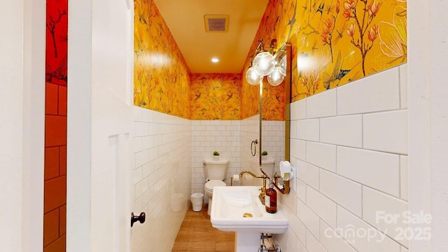 bathroom featuring toilet, a sink, visible vents, and tile walls