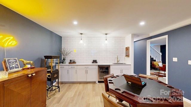 kitchen featuring wine cooler, a sink, white cabinetry, hanging light fixtures, and light countertops