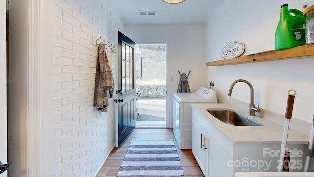 laundry room featuring cabinet space, visible vents, washer and clothes dryer, brick wall, and a sink