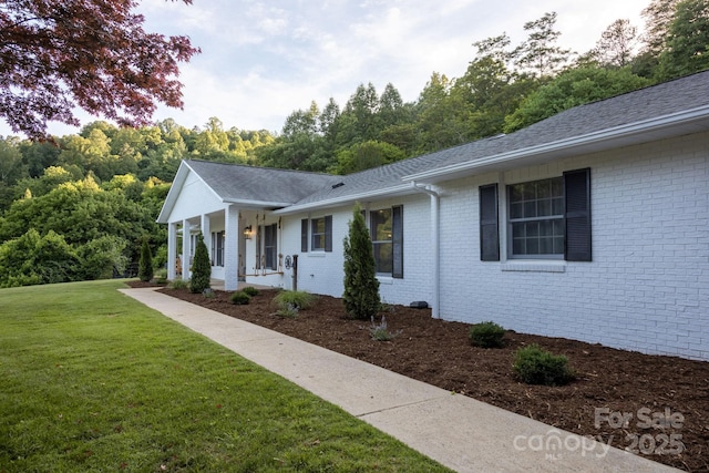 view of front of house with a front yard, covered porch, brick siding, and roof with shingles