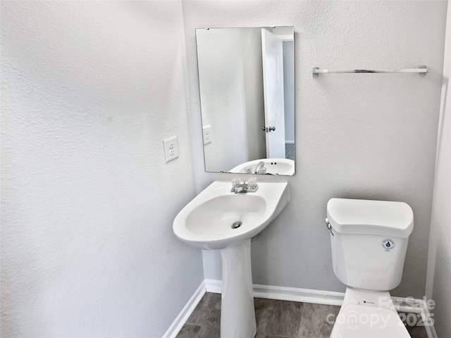 half bathroom with toilet, baseboards, and wood finished floors