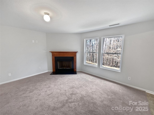 unfurnished living room with a fireplace with flush hearth, visible vents, carpet floors, and baseboards