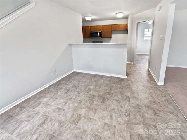 kitchen with brown cabinets, light countertops, stainless steel microwave, a peninsula, and baseboards