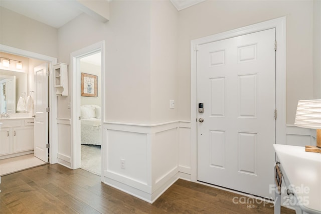 entrance foyer with beam ceiling, a decorative wall, dark wood-type flooring, and wainscoting