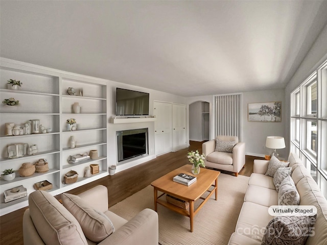 living area featuring baseboards, a fireplace, arched walkways, and dark wood-style flooring