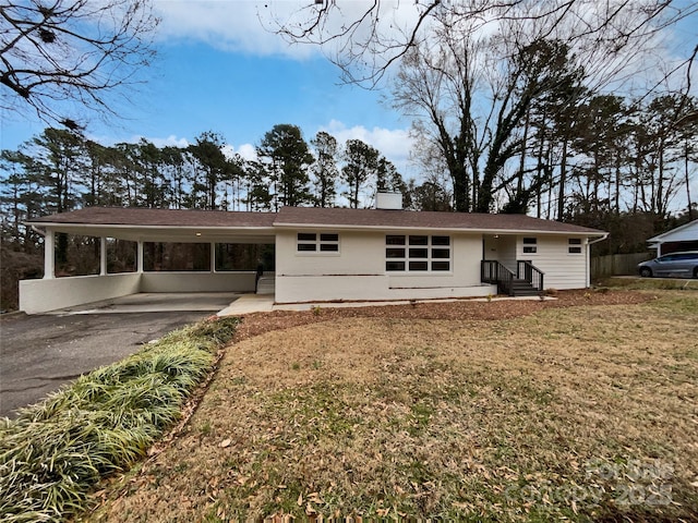 back of house featuring a carport, aphalt driveway, a chimney, and a lawn