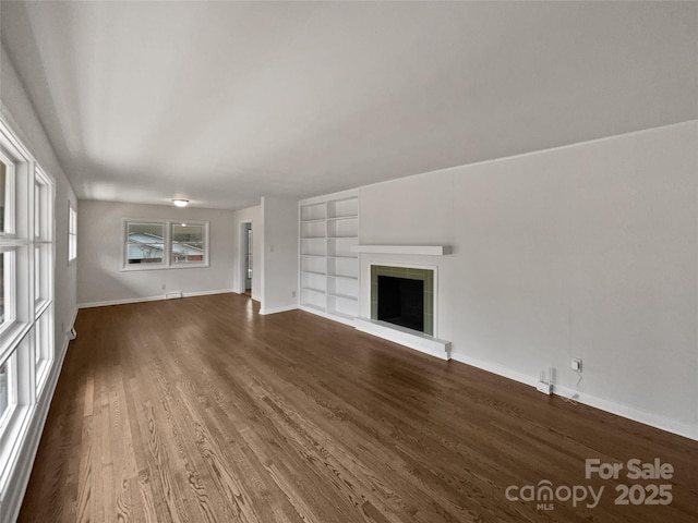 unfurnished living room with baseboards, a fireplace, built in features, and wood finished floors