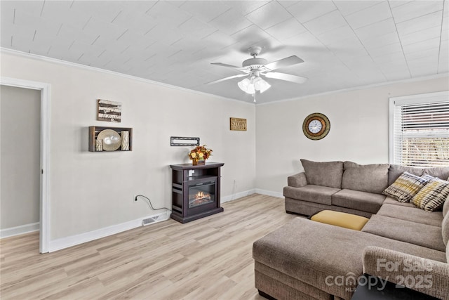 living area featuring ornamental molding, a glass covered fireplace, light wood-type flooring, and baseboards