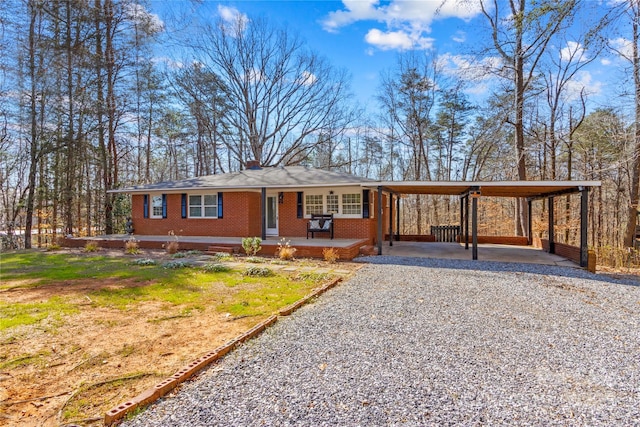 ranch-style house featuring gravel driveway, a porch, an attached carport, and brick siding