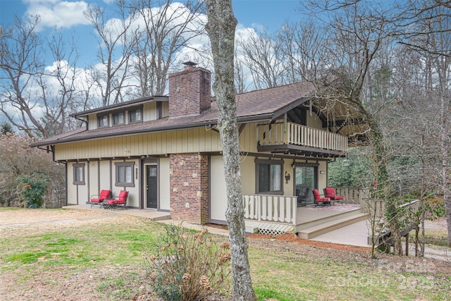 back of house with brick siding, a chimney, a shingled roof, a lawn, and a balcony