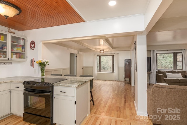 kitchen with light wood finished floors, open floor plan, wainscoting, white cabinetry, and black range with electric cooktop