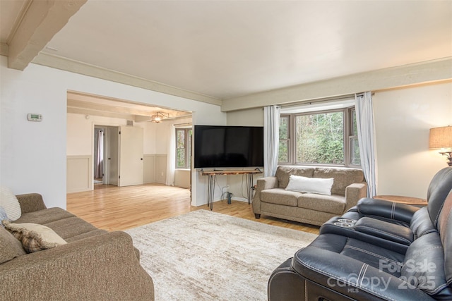 living area with light wood-style floors, a wainscoted wall, and beamed ceiling