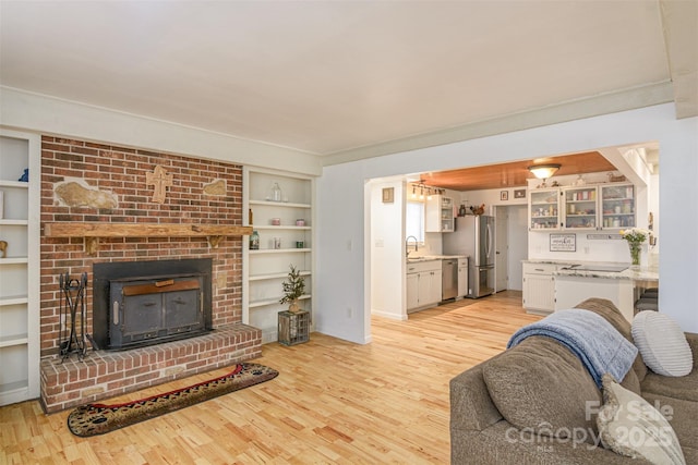 living room featuring light wood-type flooring, built in shelves, ornamental molding, and a fireplace