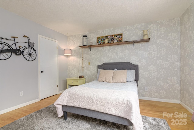 bedroom with wood finished floors, a textured ceiling, baseboards, and wallpapered walls