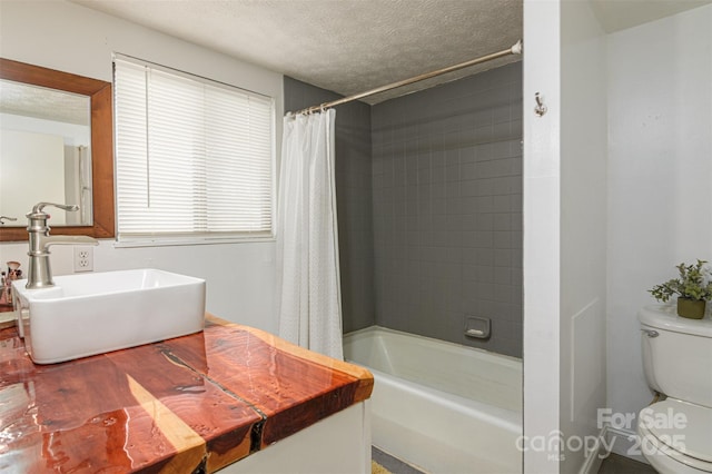 bathroom featuring toilet, shower / bath combination with curtain, a textured ceiling, and a sink