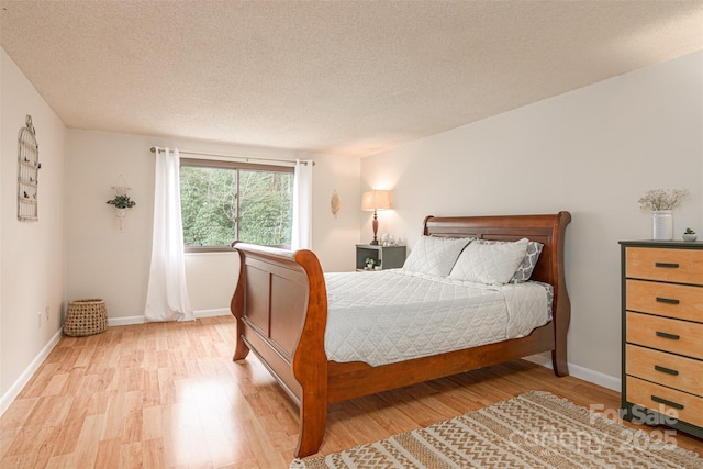 bedroom with light wood-style floors, baseboards, and a textured ceiling