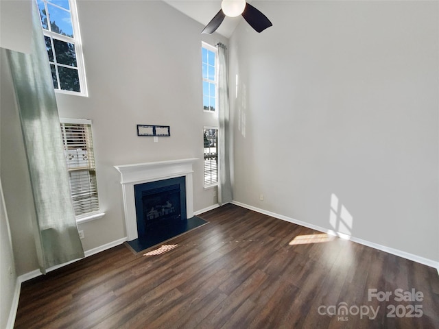 unfurnished living room featuring a towering ceiling, a fireplace, baseboards, and wood finished floors