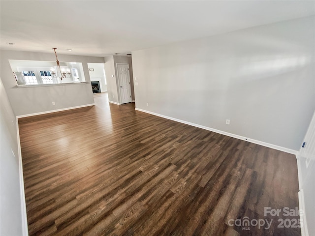 unfurnished living room with a chandelier, dark wood-style flooring, a fireplace, and baseboards