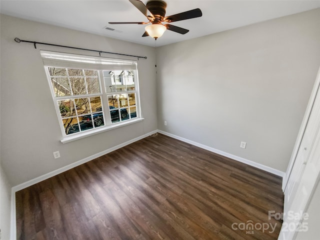 spare room with dark wood-style floors, a ceiling fan, visible vents, and baseboards