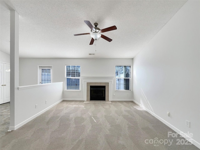 unfurnished living room with a wealth of natural light, visible vents, a textured ceiling, and a tiled fireplace