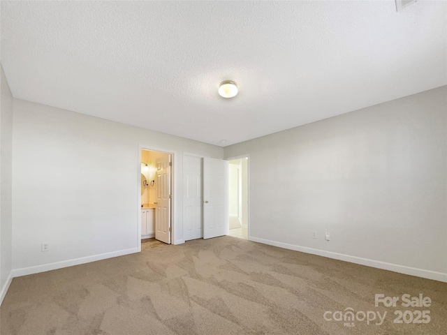 unfurnished bedroom featuring carpet floors, ensuite bath, a textured ceiling, and baseboards