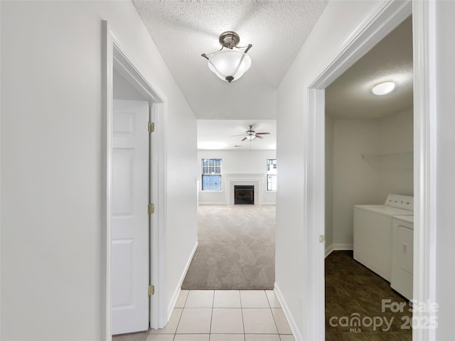 hallway with light carpet, light tile patterned floors, washer and clothes dryer, and a textured ceiling