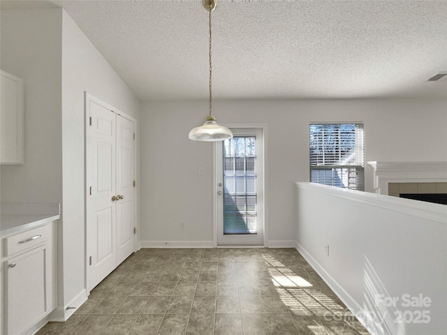 unfurnished dining area featuring a textured ceiling, a fireplace, visible vents, and baseboards