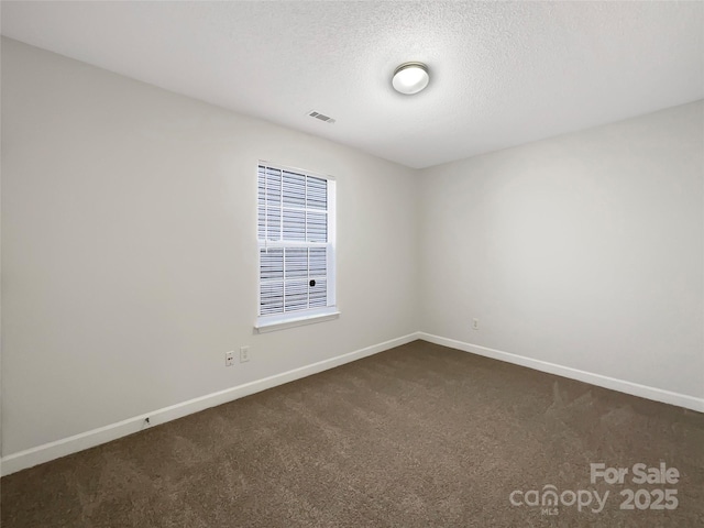 empty room with a textured ceiling, dark colored carpet, visible vents, and baseboards