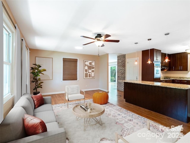 living room with light wood finished floors, a ceiling fan, and baseboards