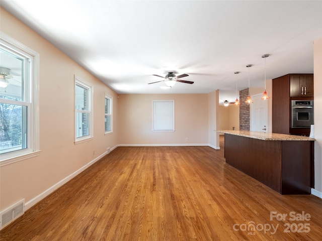 interior space featuring visible vents, a ceiling fan, oven, hanging light fixtures, and light wood-style floors