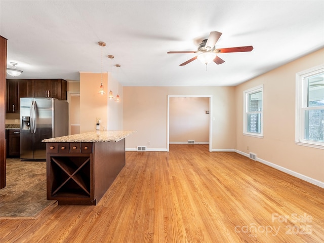 kitchen with dark brown cabinetry, visible vents, a center island, light wood-style floors, and stainless steel refrigerator with ice dispenser