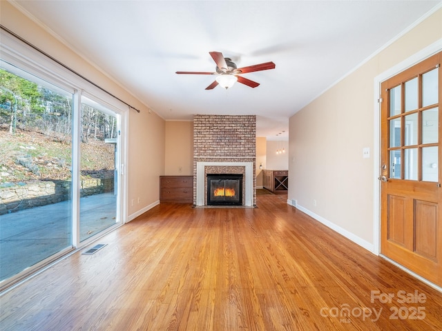 unfurnished living room featuring light wood-style floors, a brick fireplace, visible vents, and ornamental molding