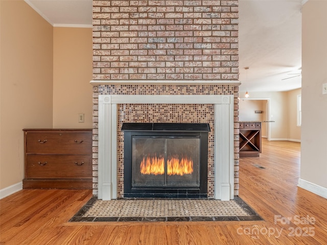 room details featuring crown molding, baseboards, wood finished floors, and a glass covered fireplace