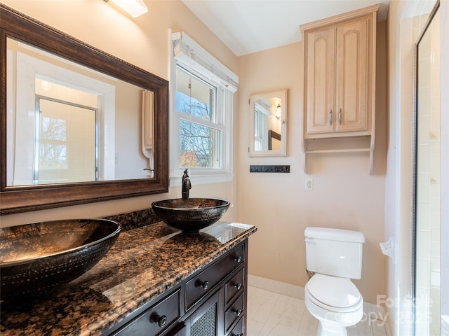 full bath with double vanity, baseboards, toilet, marble finish floor, and a sink