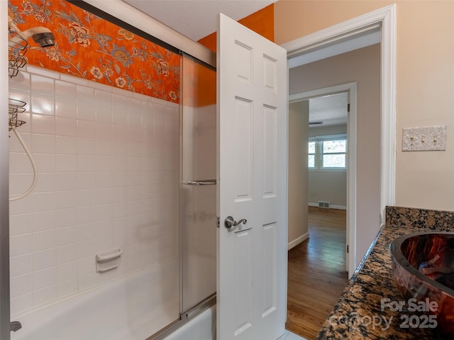 full bathroom featuring wallpapered walls, baseboards, visible vents, shower / bath combination with glass door, and wood finished floors