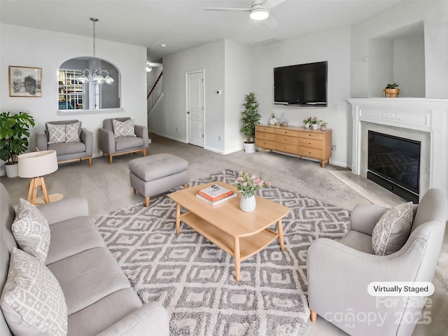 living room with ceiling fan with notable chandelier, carpet floors, a fireplace, baseboards, and stairs