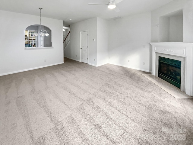 unfurnished living room with stairs, a high end fireplace, baseboards, and ceiling fan with notable chandelier