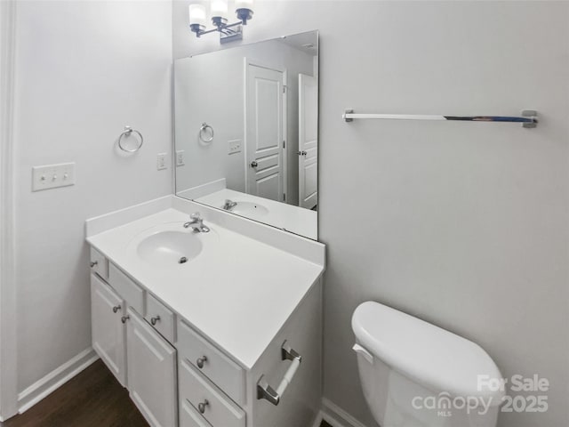 half bath with baseboards, vanity, toilet, and wood finished floors