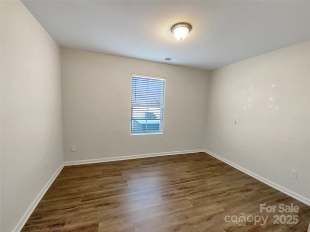 spare room with baseboards and wood finished floors