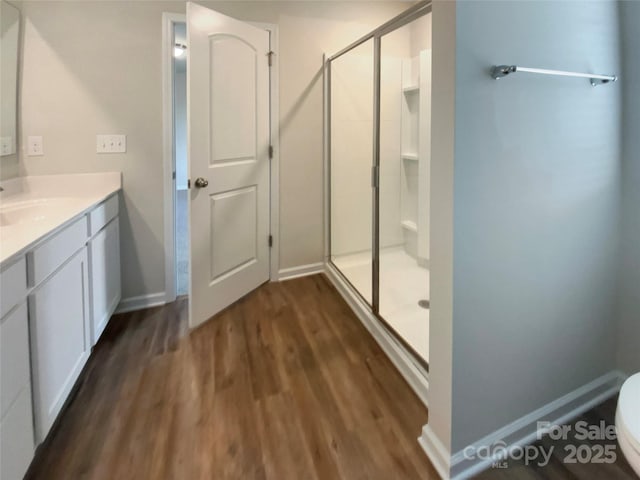 bathroom featuring a stall shower, baseboards, toilet, wood finished floors, and vanity