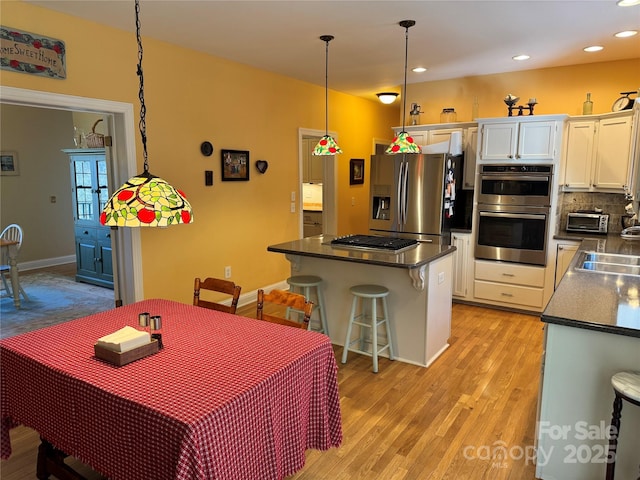 kitchen with hanging light fixtures, a breakfast bar, white cabinetry, and stainless steel appliances