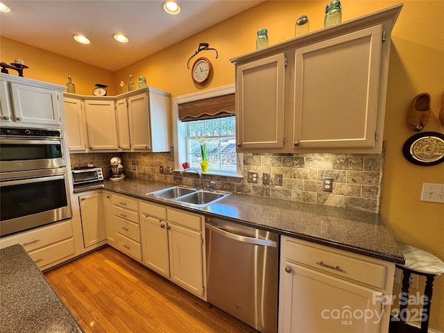 kitchen featuring stainless steel appliances, dark countertops, a sink, and backsplash