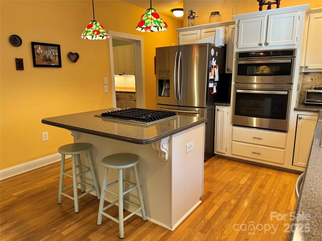 kitchen with appliances with stainless steel finishes, white cabinets, a breakfast bar area, and pendant lighting