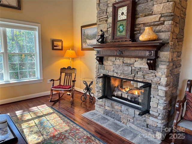 sitting room featuring dark wood-style floors, baseboards, and a stone fireplace