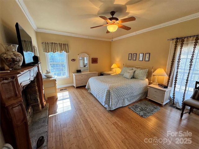 bedroom featuring visible vents, ceiling fan, crown molding, light wood-style floors, and a fireplace