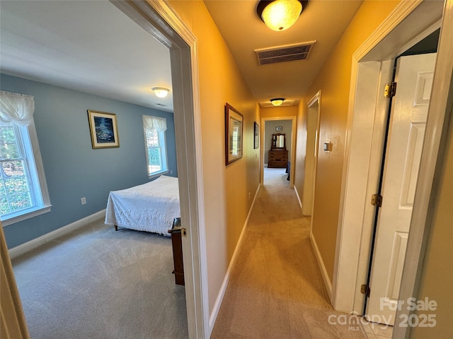 hall with baseboards, visible vents, and light colored carpet