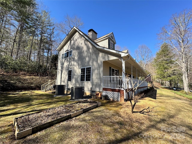 view of side of home featuring a yard, a chimney, cooling unit, and a garden