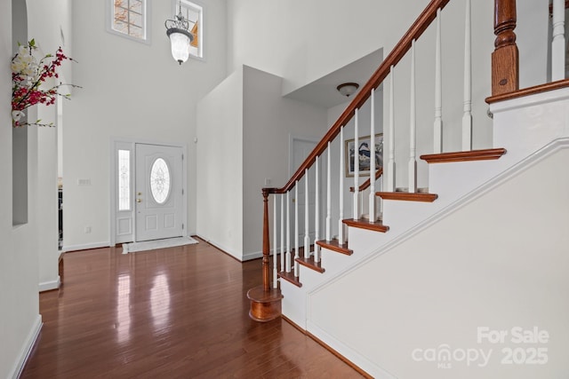 entrance foyer with dark wood-style floors, stairs, a high ceiling, and baseboards