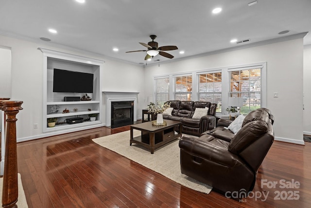 living area featuring dark wood-style floors, a fireplace with flush hearth, visible vents, and crown molding